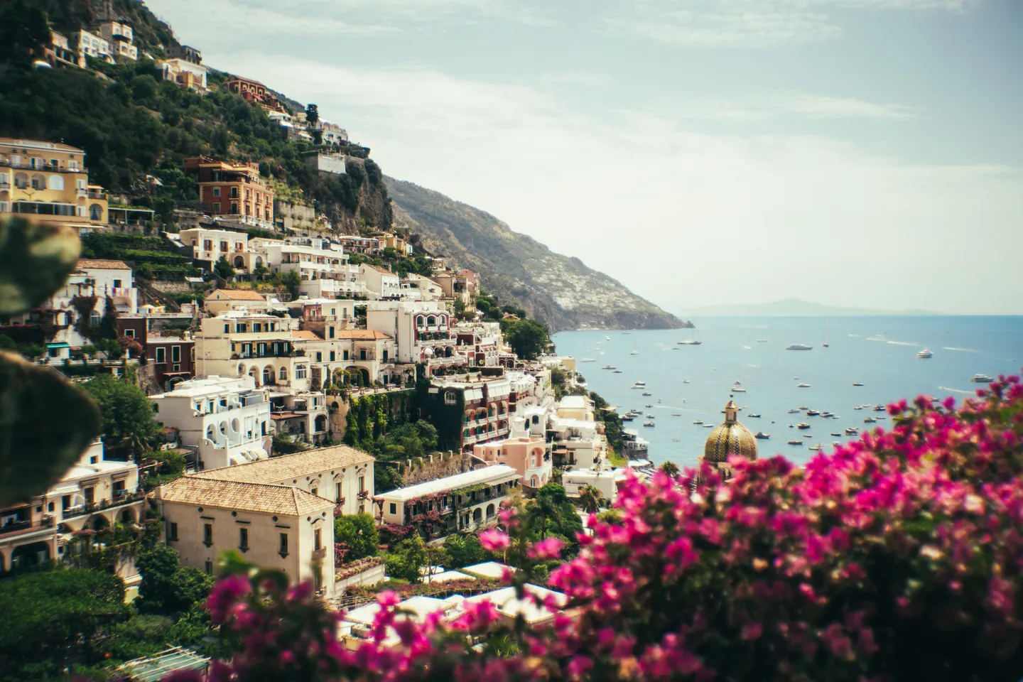 Sunlit Positano hillside above the sea, framed by pink bougainvillea